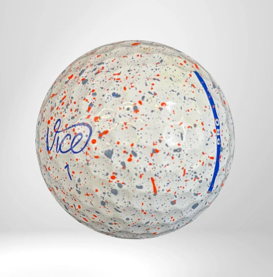 Weißer Golfball mit blauem Logo, roten und grauen Farbsprenkeln auf hellem Hintergrund