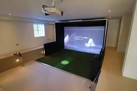 Moderner Indoor Golf Simulator mit Leinwand, Projektor und grünem Abschlagbereich in hellem Raum