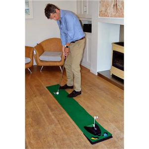 Mann spielt Golf auf grünem Indoor Putting Mat mit Ballrücklauf auf Holzboden